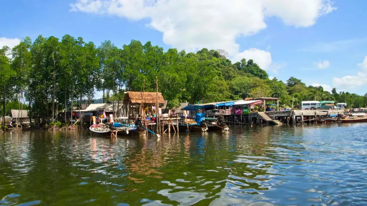 Koh Mook village beside the pier A riverside village with stilt houses, boats, and docks along a calm waterway under a blue sky